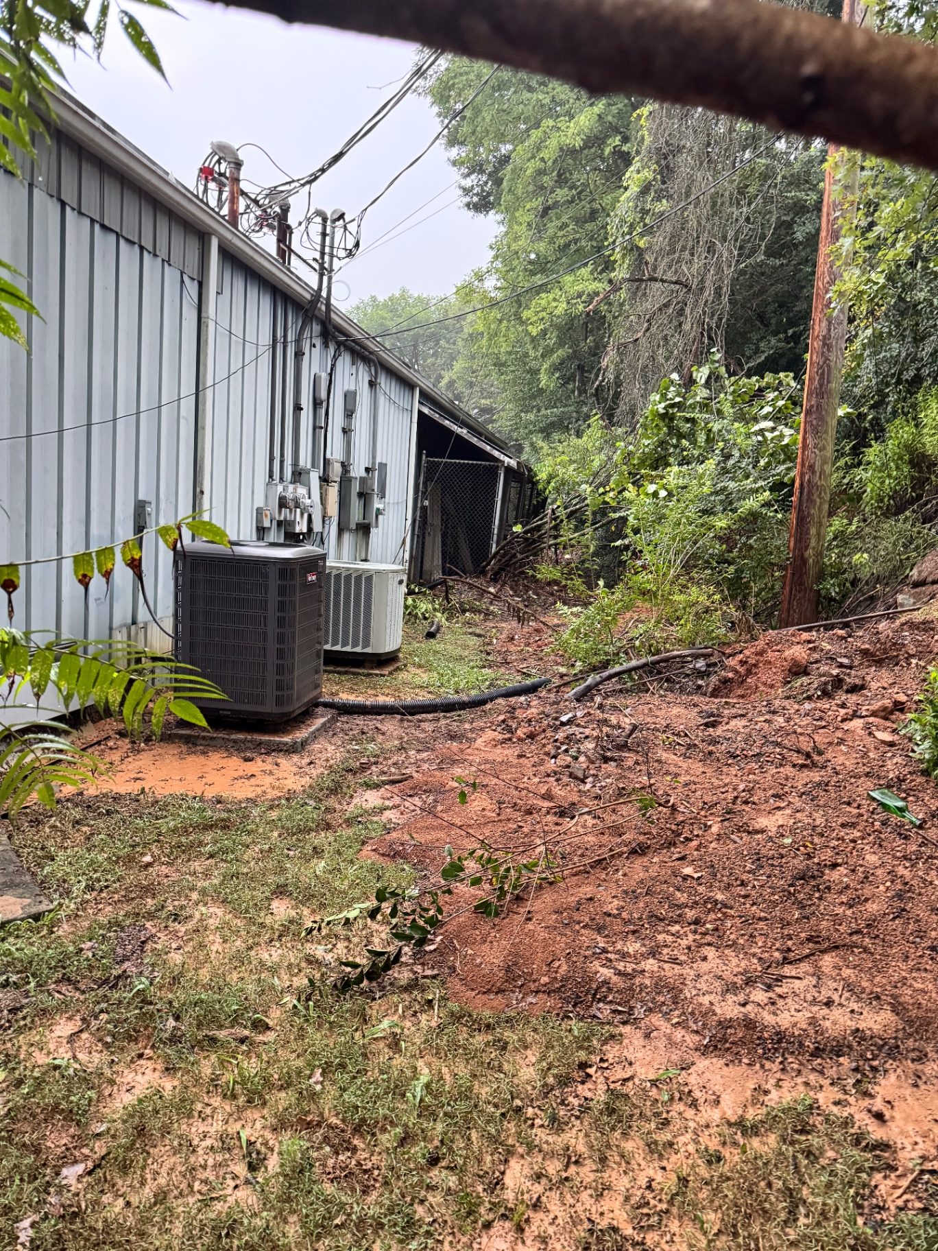 Storm washout and mud flow against the side of a commercial metal building with HVAC units and electrical service