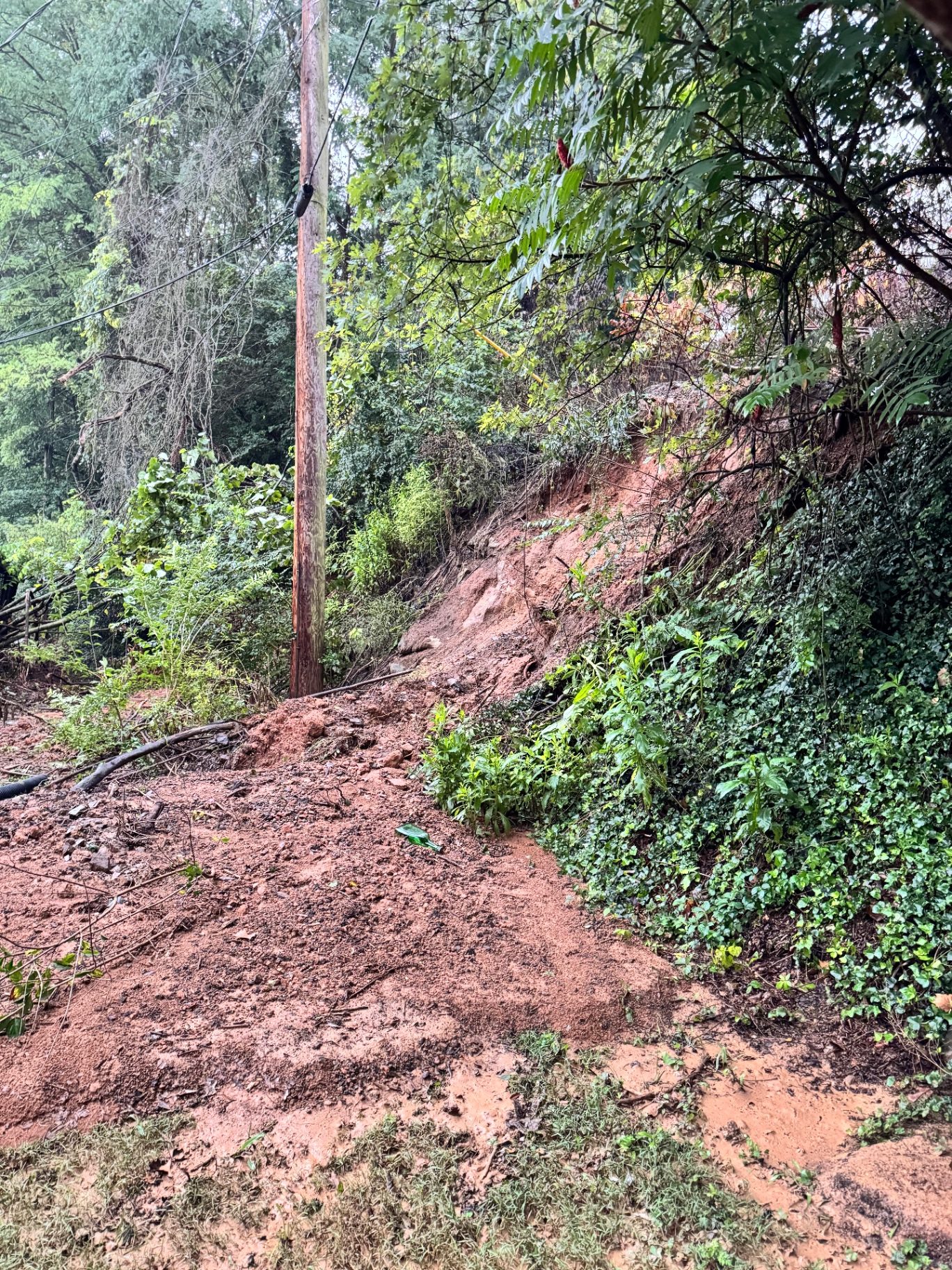 Collapsed embankment and slide material around a leaning utility pole after heavy rain