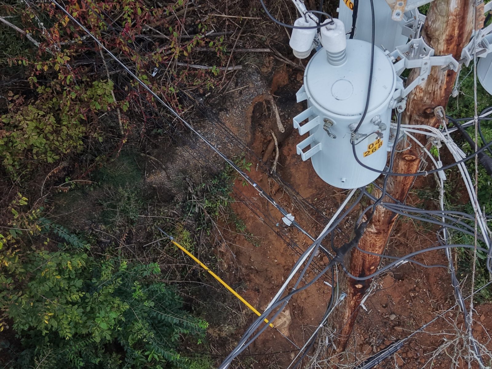 Close-range drone view of a pole-mounted transformer with conductors above an eroded hillside