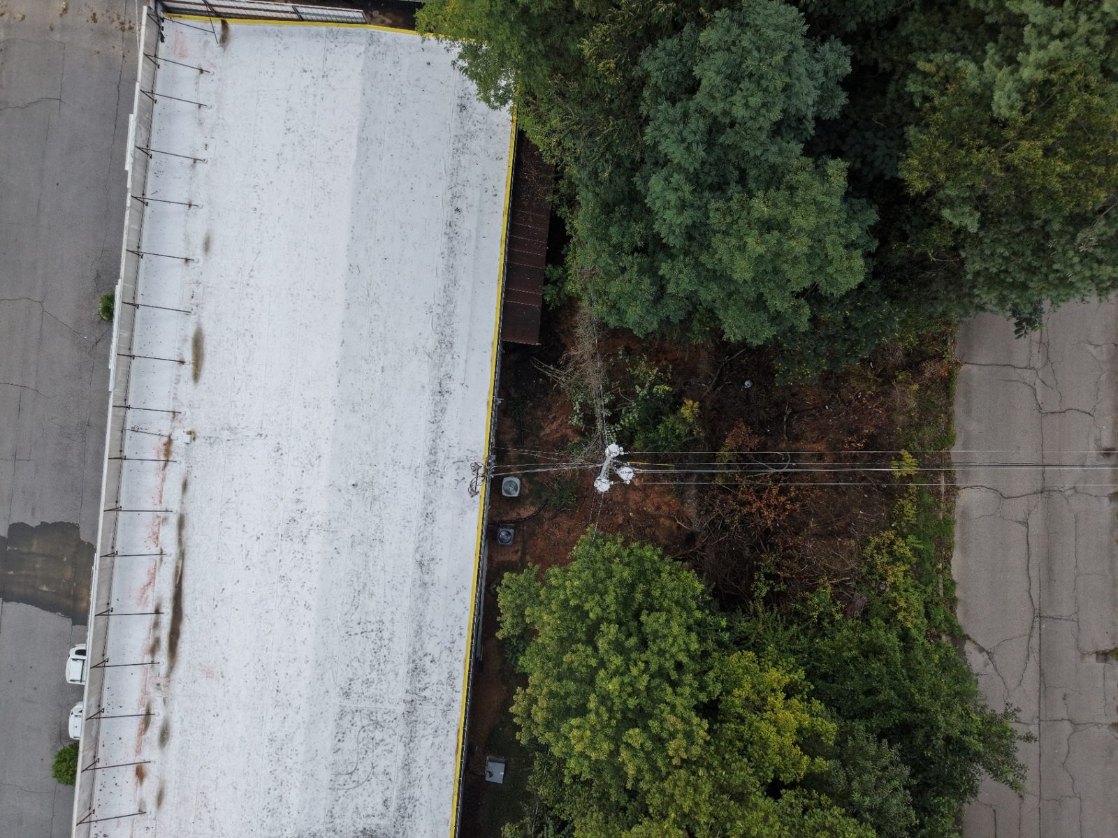 Top-down drone photo of a commercial flat roof next to a storm-eroded right-of-way and power lines