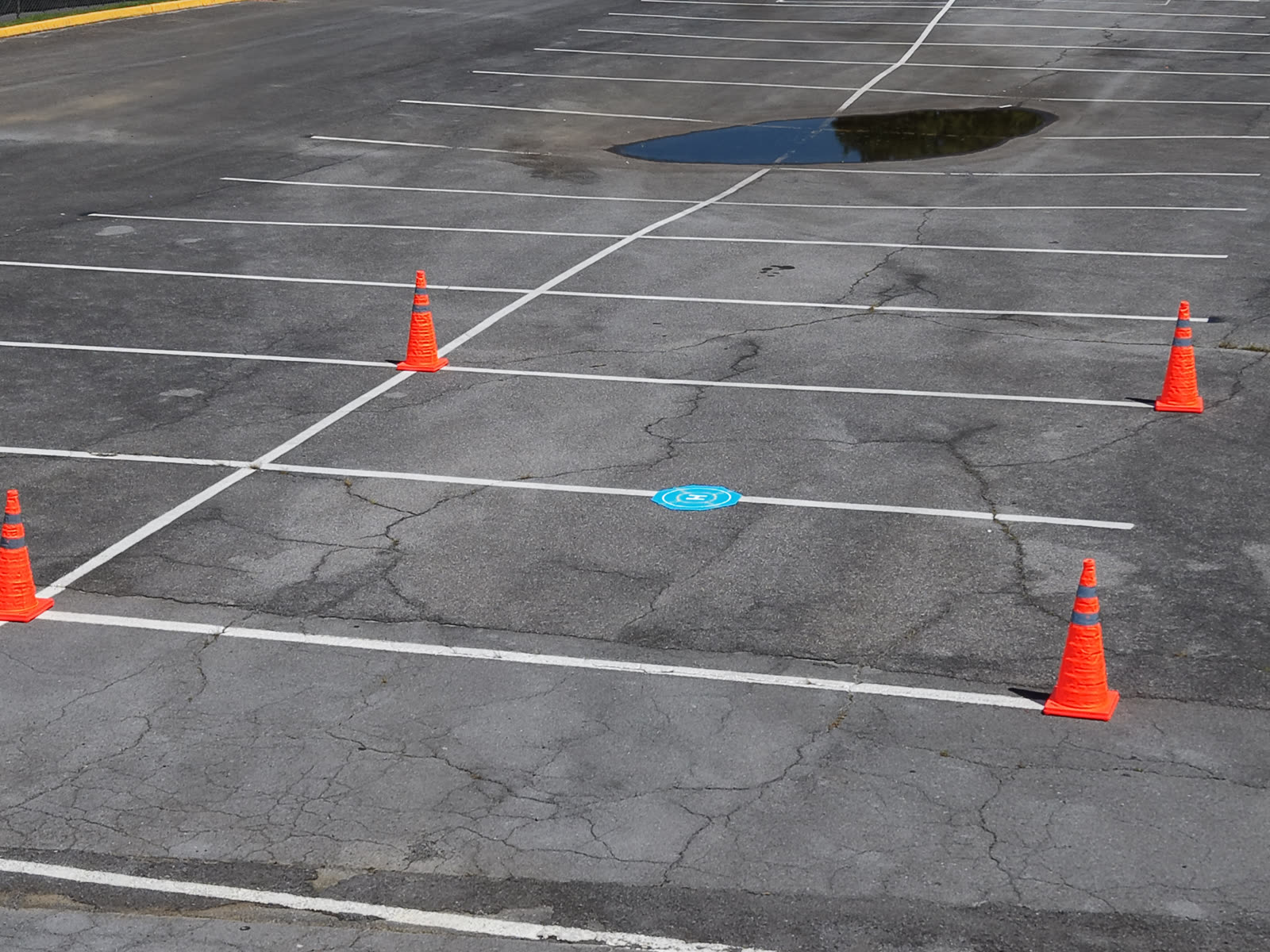 Aerial view of a marked drone landing pad surrounded by orange safety cones in a cordoned section of a parking lot